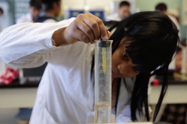 Student in lab coat dropping liquid into beaker